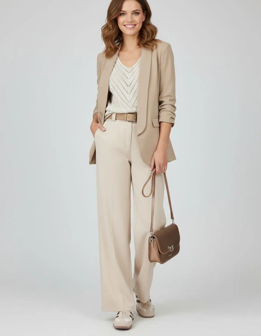 Model wearing a cream V-neck knit top and wide-leg pants, carrying a brown handbag.