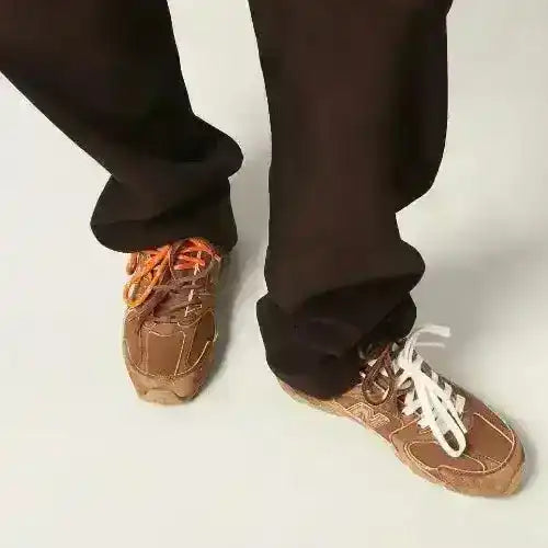 Brown low-top sneakers with orange laces and textured panels.