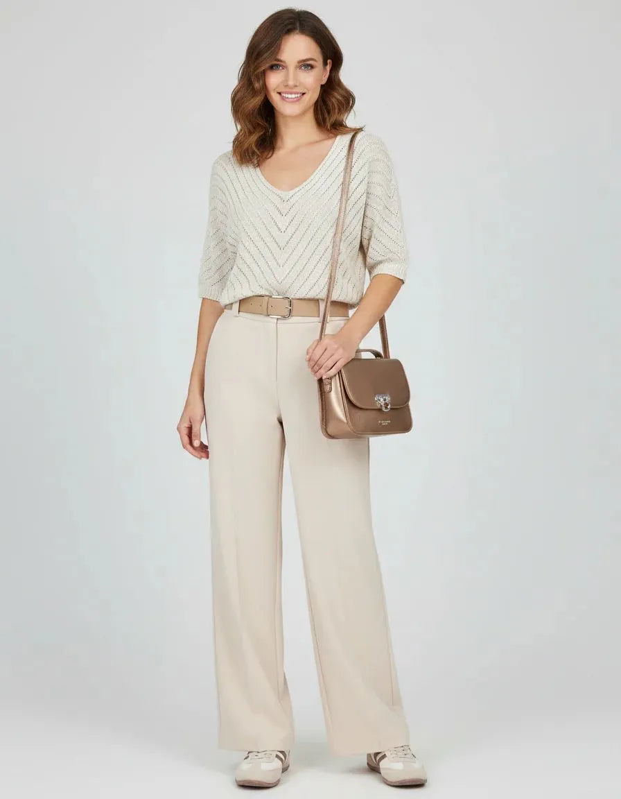 Model wearing a cream V-neck knit top and wide-leg pants, carrying a brown handbag.