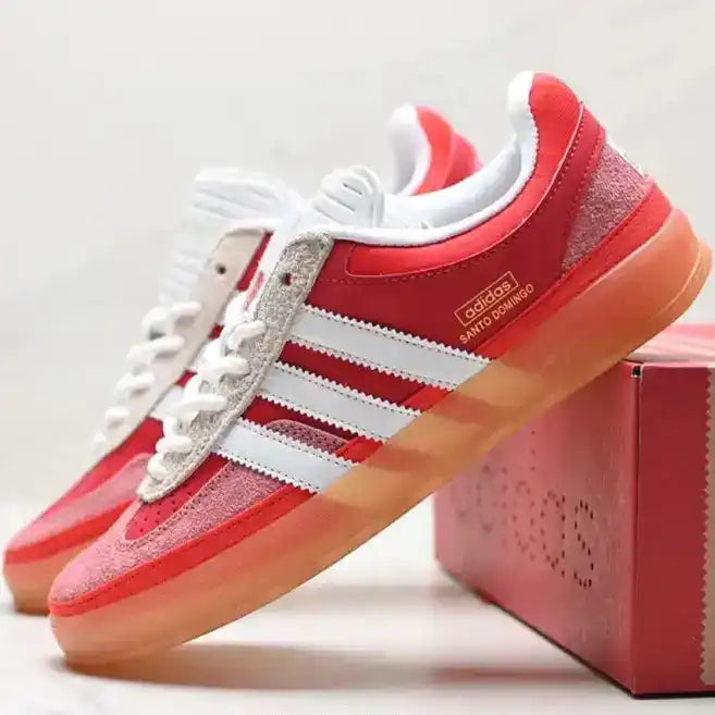 Red Adidas sneakers with white stripes on a light gray background