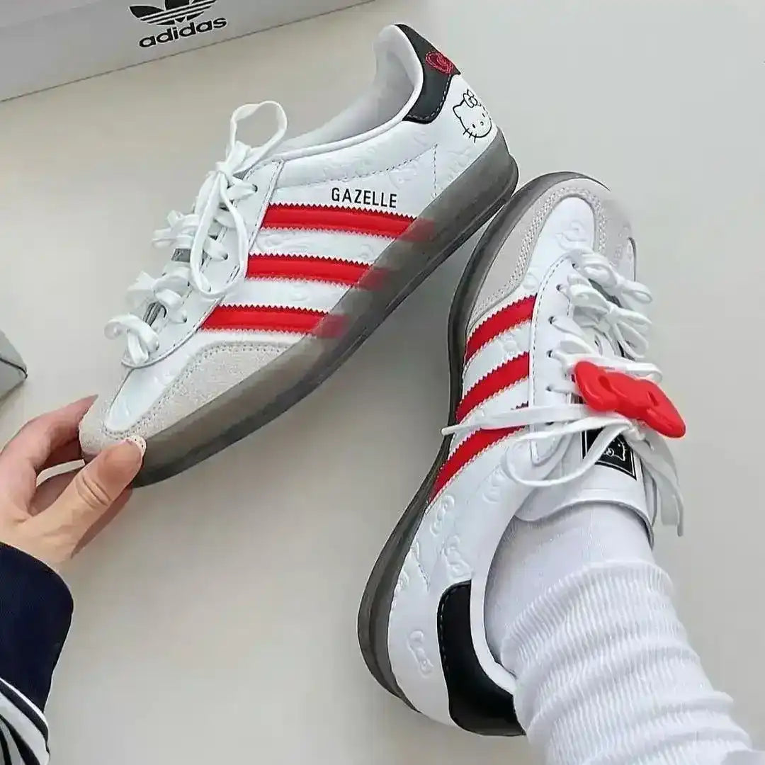 White sneakers with red stripes and black soles held by a hand against a white background