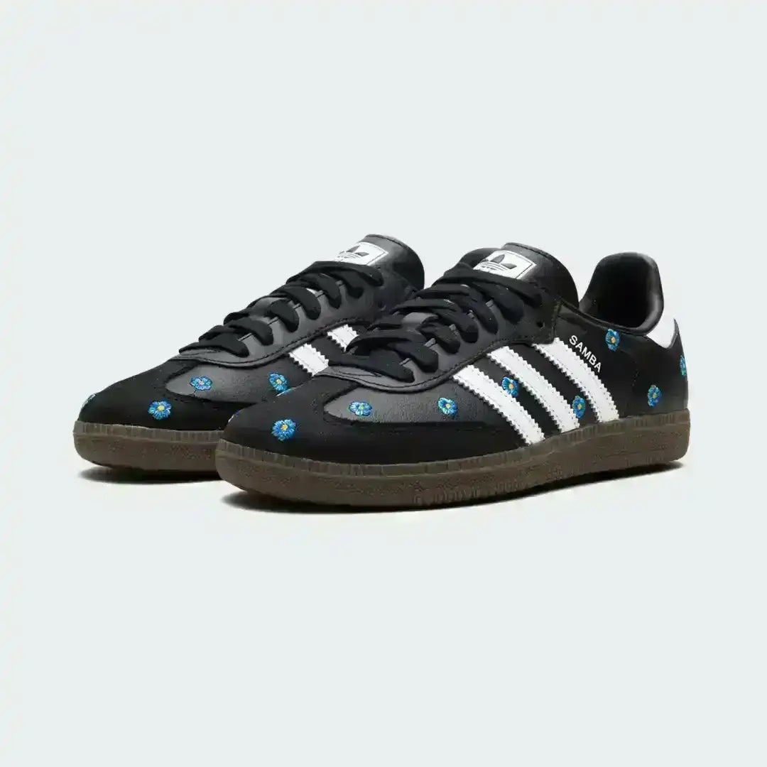 Black Adidas Samba shoes featuring delicate blue flower embroidery, signature white triple stripes, premium leather build and a sturdy gum outsole.