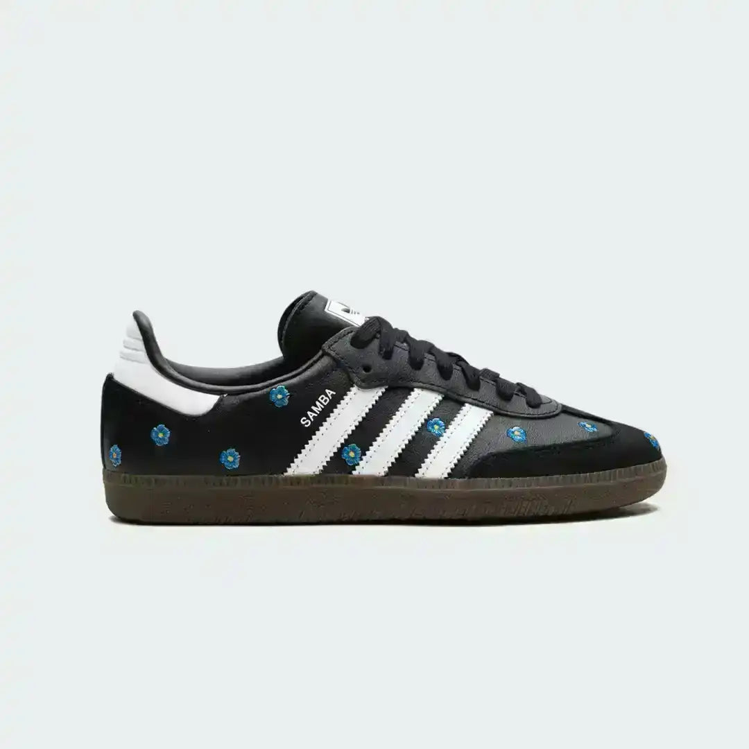 Black leather Adidas Samba sneakers decorated with blue flower embroidery, iconic white stripes and a classic gum outsole for retro appeal.