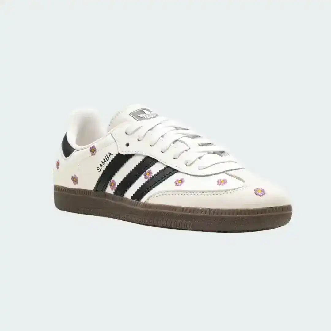 White Adidas Samba shoes featuring pink flower embroidery, signature black stripes, premium leather upper and a sleek dark gum outsole.