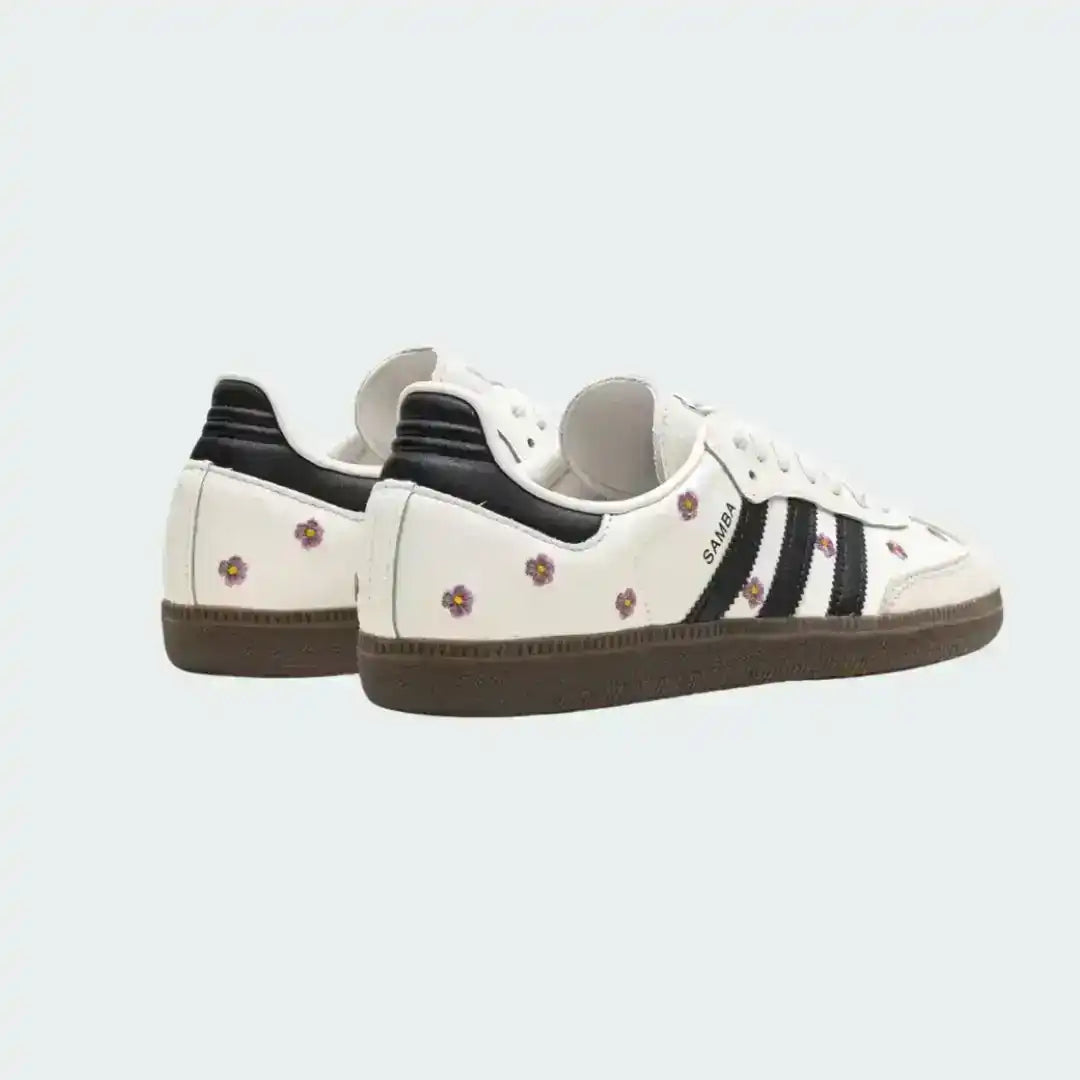 Adidas Samba white sneakers decorated with pink flowers, contrasted by black stripes and finished with a sturdy dark gum outsole.