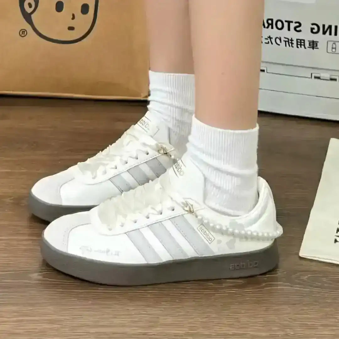 Adidas sneakers in white leather with grey stripes, a pearl ankle accessory and a dark gum sole, designed for comfortable and elegant wear.