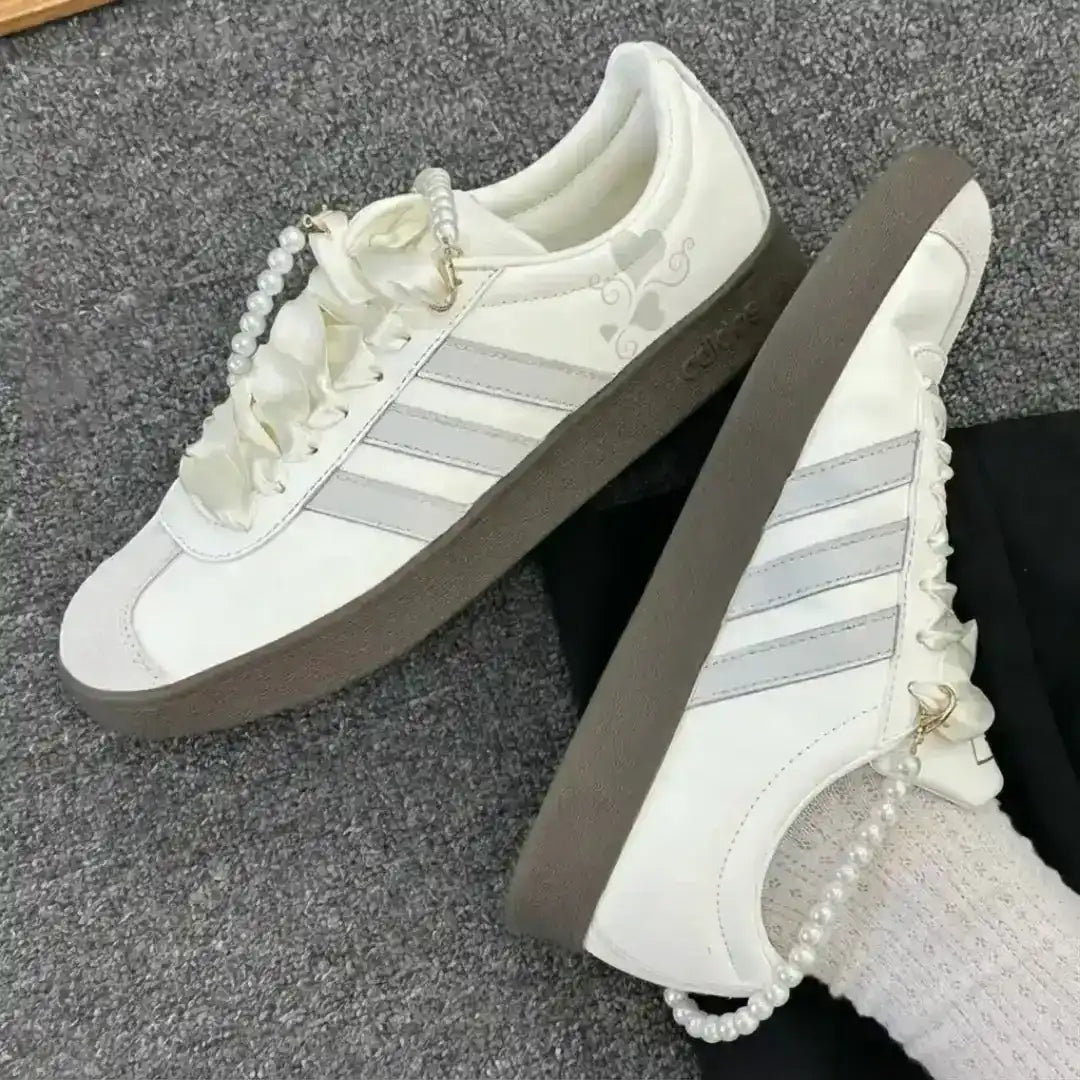 White Adidas lifestyle sneakers featuring grey detailing and a pearl ankle bracelet, paired with a textured dark gum sole for unique style.