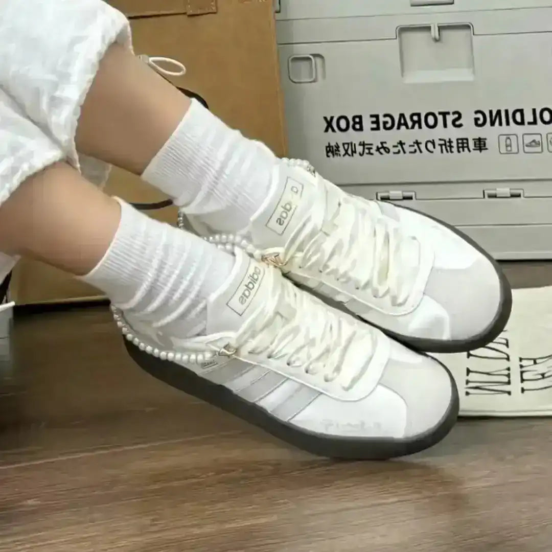 Adidas white sneakers featuring grey stripes, a pearl ankle chain and a dark gum sole that blends sporty comfort with delicate accessories.