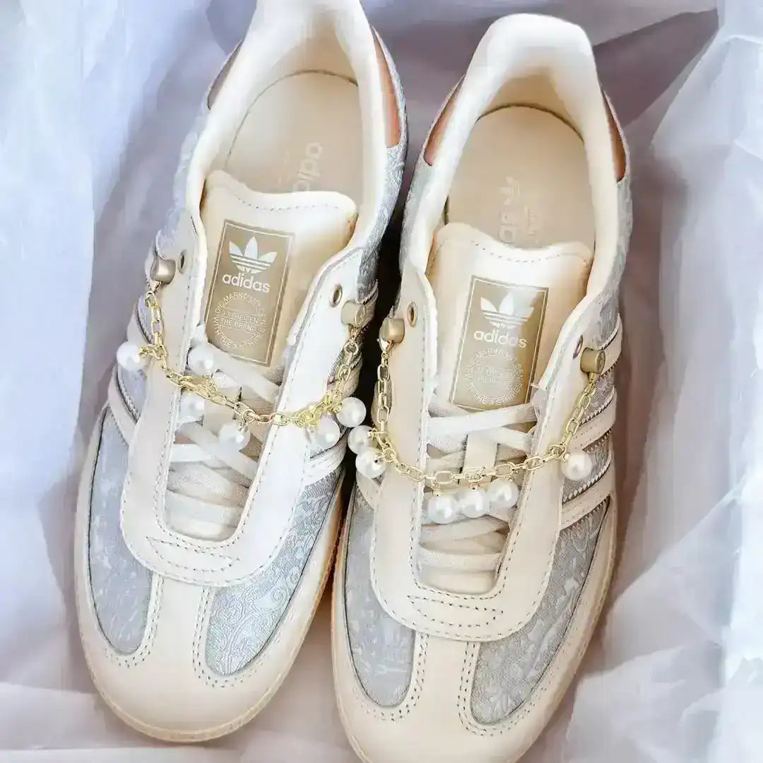 Beige Adidas shoes with decorative pearl-and-chain accents, textured paneling and smooth leather components forming a chic lifestyle design.