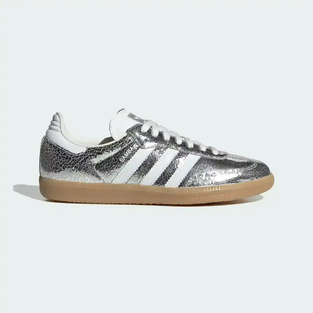 Close up detail of Adidas Samba Metallic sneaker showing liquid silver leather texture, black three stripes, and suede T-toe