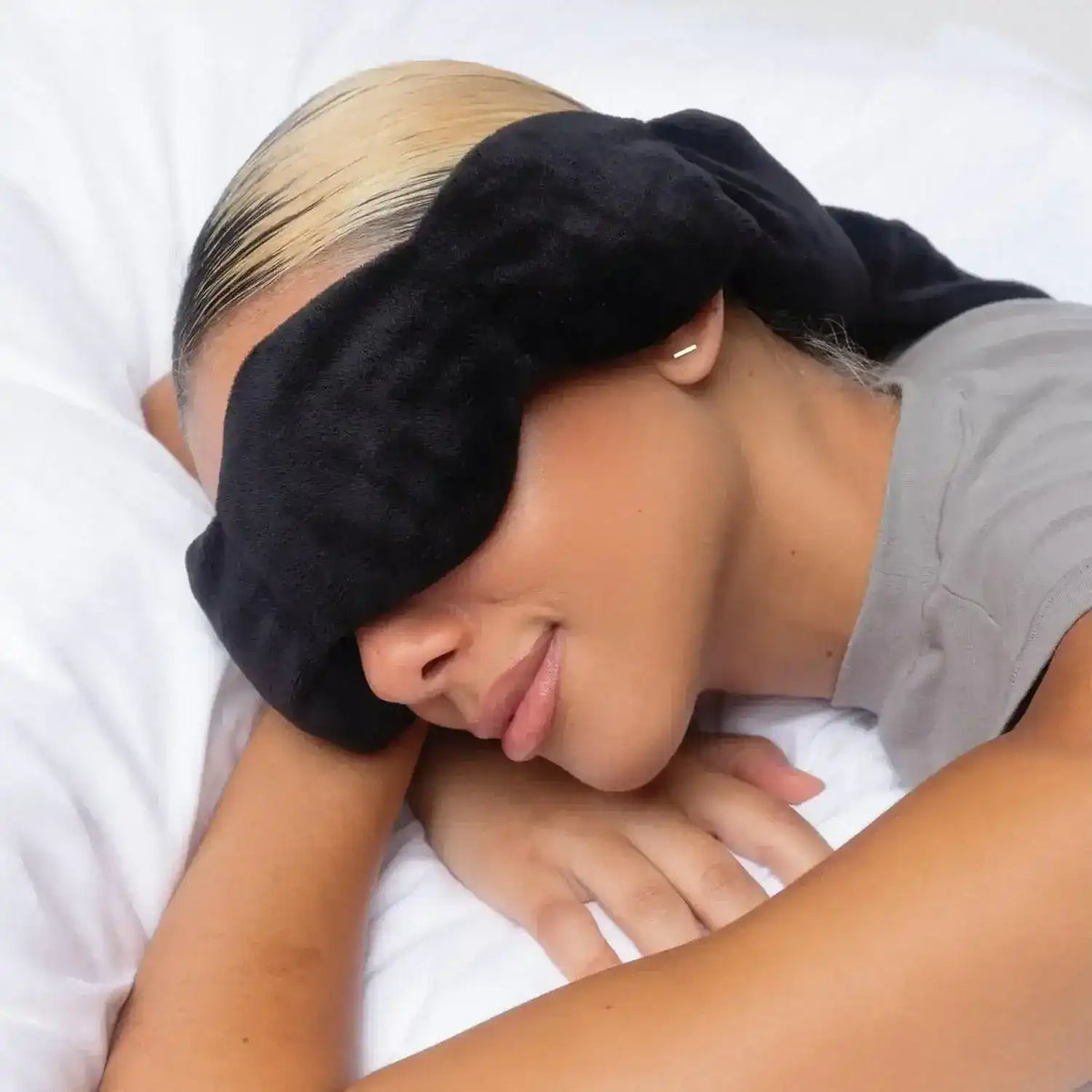 Person resting on a pillow while wearing a black sleep mask.