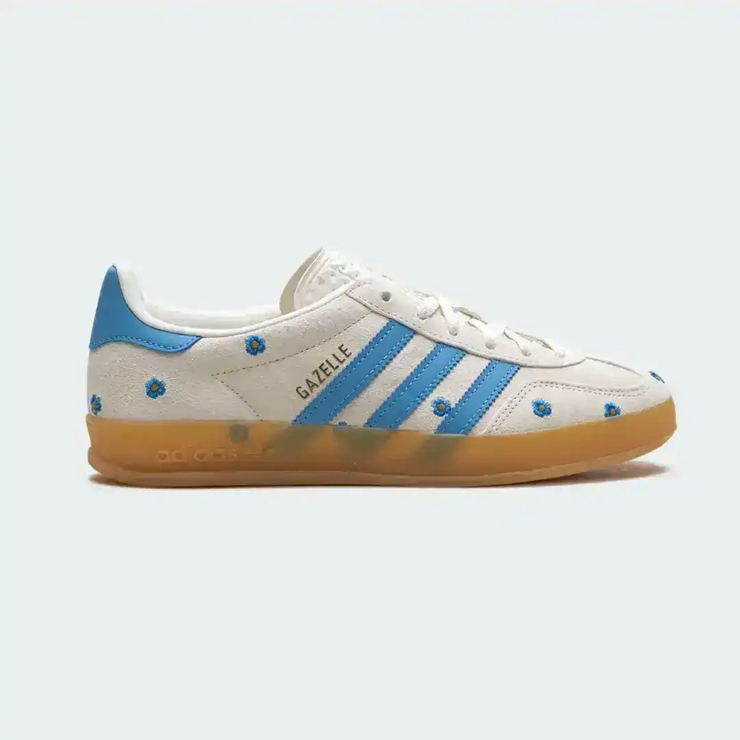 Stylish Adidas Gazelle sneakers in white suede with bright blue stripes, floral blue embroidery, and a durable translucent gum sole for comfort.
