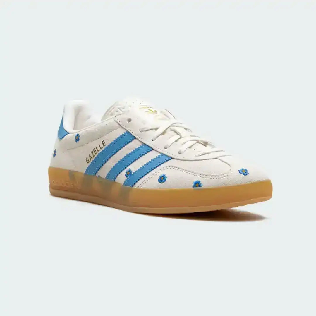 Adidas Gazelle crafted in white suede with elegant blue flower details, signature blue stripes and a warm gum outsole offering vintage appeal.
