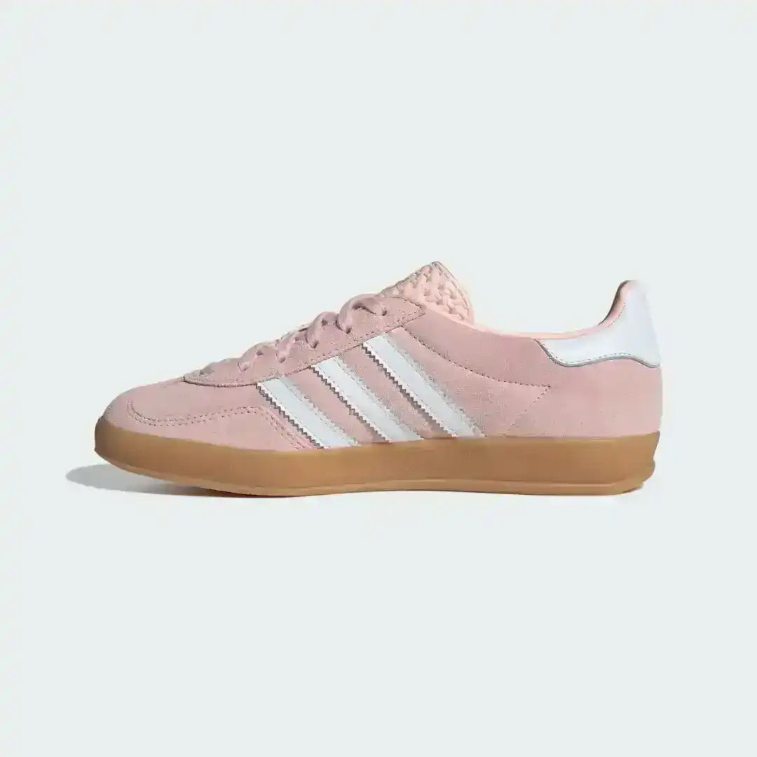 Adidas Gazelle Indoor sneakers in a vibrant pink and white color scheme, featuring a low-profile silhouette and a distinct dark gum midsole that wraps up the side.