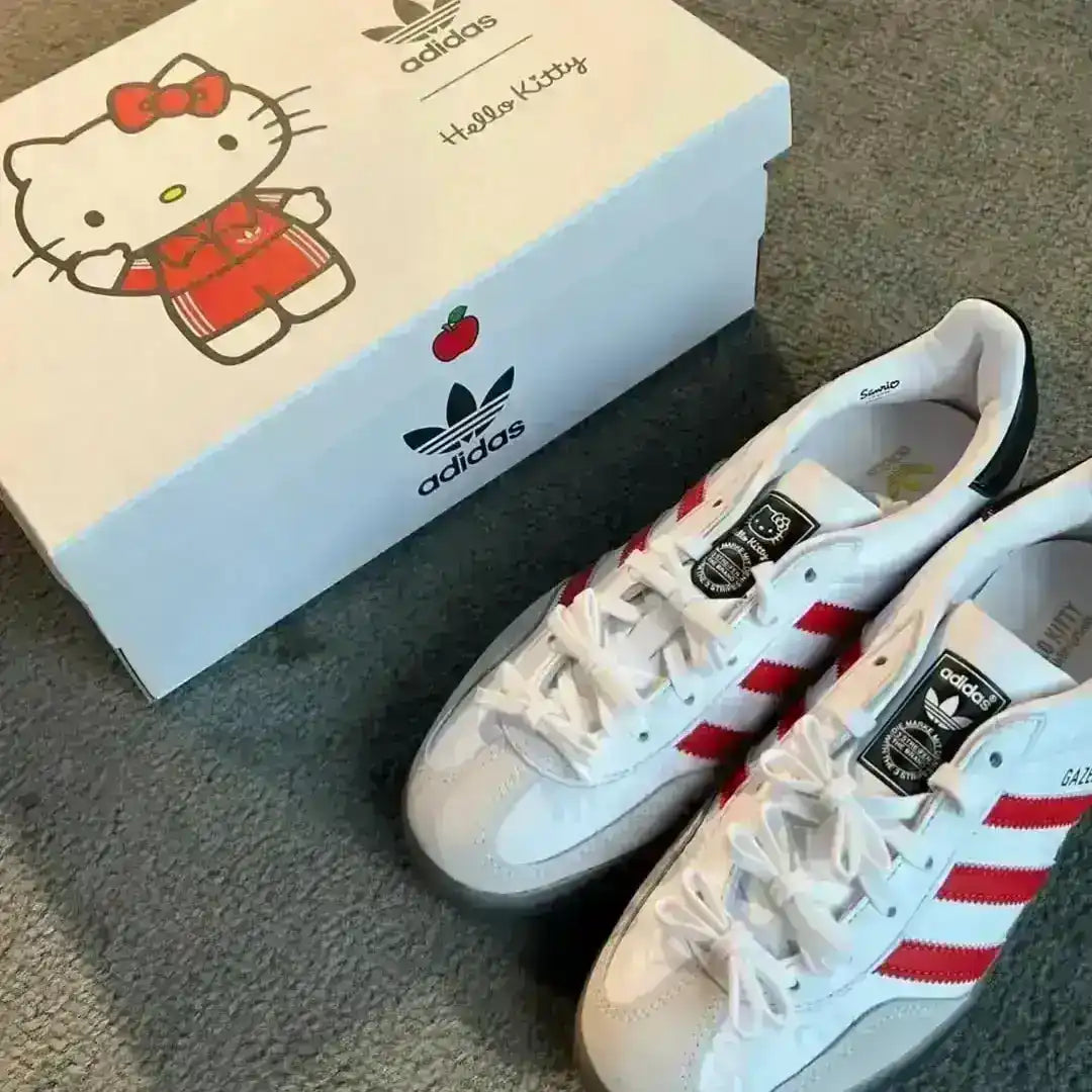 Collectible Adidas Gazelle Indoor Hello Kitty White/Red sneakers featuring a grey suede toe box, custom ribbon-style laces, and a distinct Hello Kitty head graphic on the rear quarter panel.