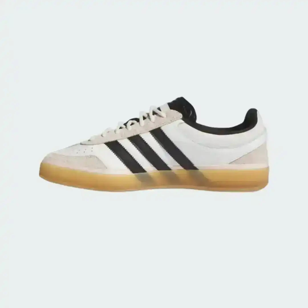 Adidas Gazelle Indoor sneakers in white leather featuring black serrated stripes, a grey suede toe overlay, and a classic translucent gum rubber outsole for a retro look.