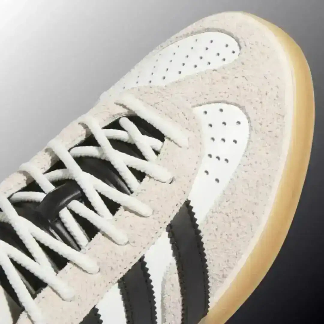 Side profile view of the Adidas Gazelle Indoor White Black Gum shoes, showing the premium leather upper, contrasting black three stripes, and gold metallic branding details.