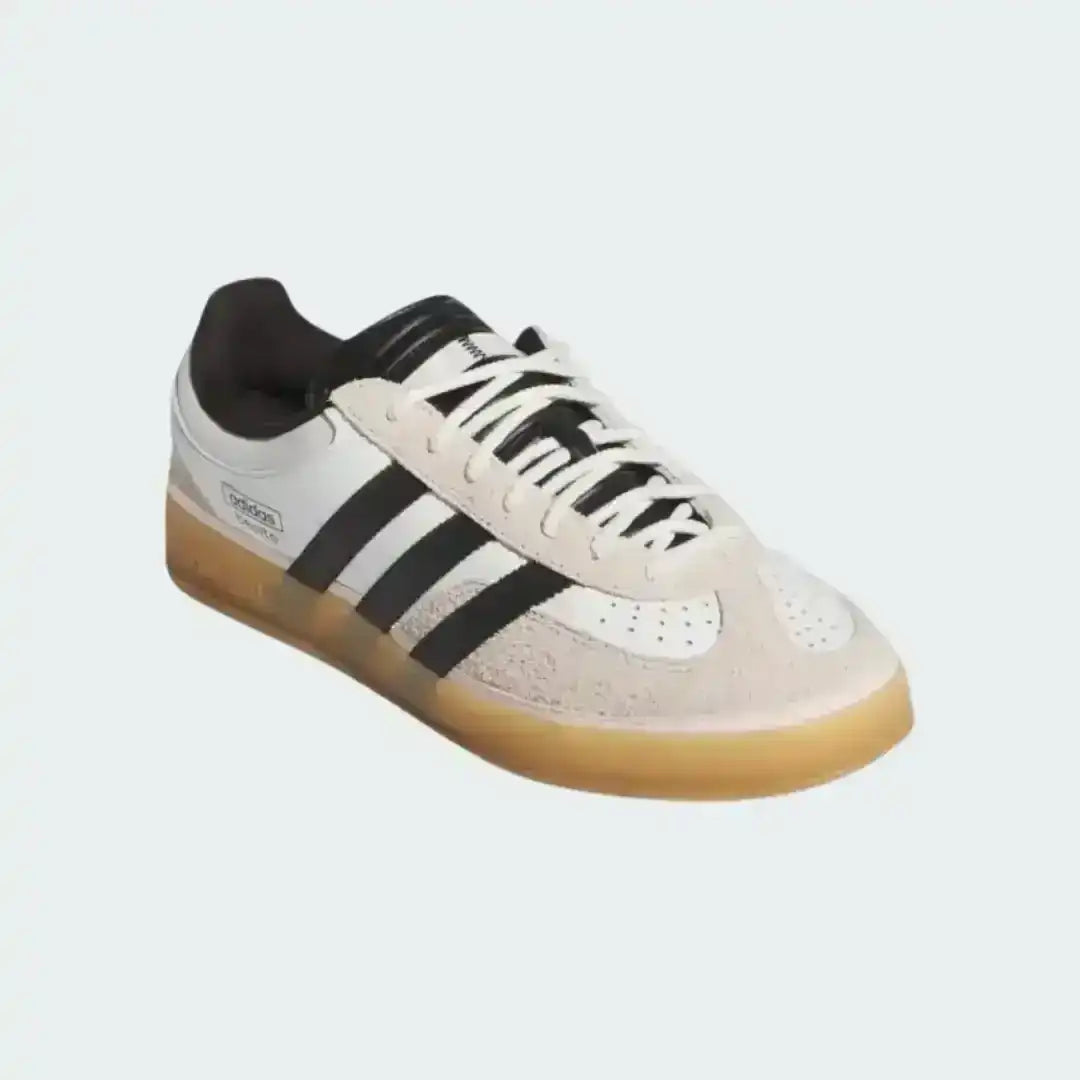 Adidas Gazelle Indoor White Black sneakers with a retro look, highlighting the gum rubber sole, black leather stripes, and gold foil 'GAZELLE' text printed on the side panel.