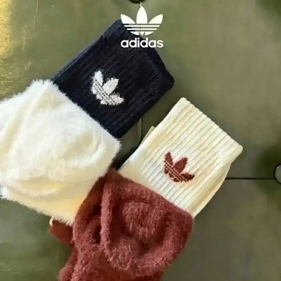High-angle view of Adidas fuzzy lounge socks, emphasizing the soft, thick material and the branding details on the cuffs of the various color options shown.