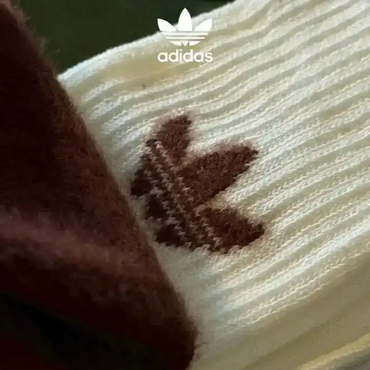 Essential Adidas cozy socks for cold weather, made from a fluffy knit fabric and featuring the classic Trefoil logo in black, white, and brown color variations.