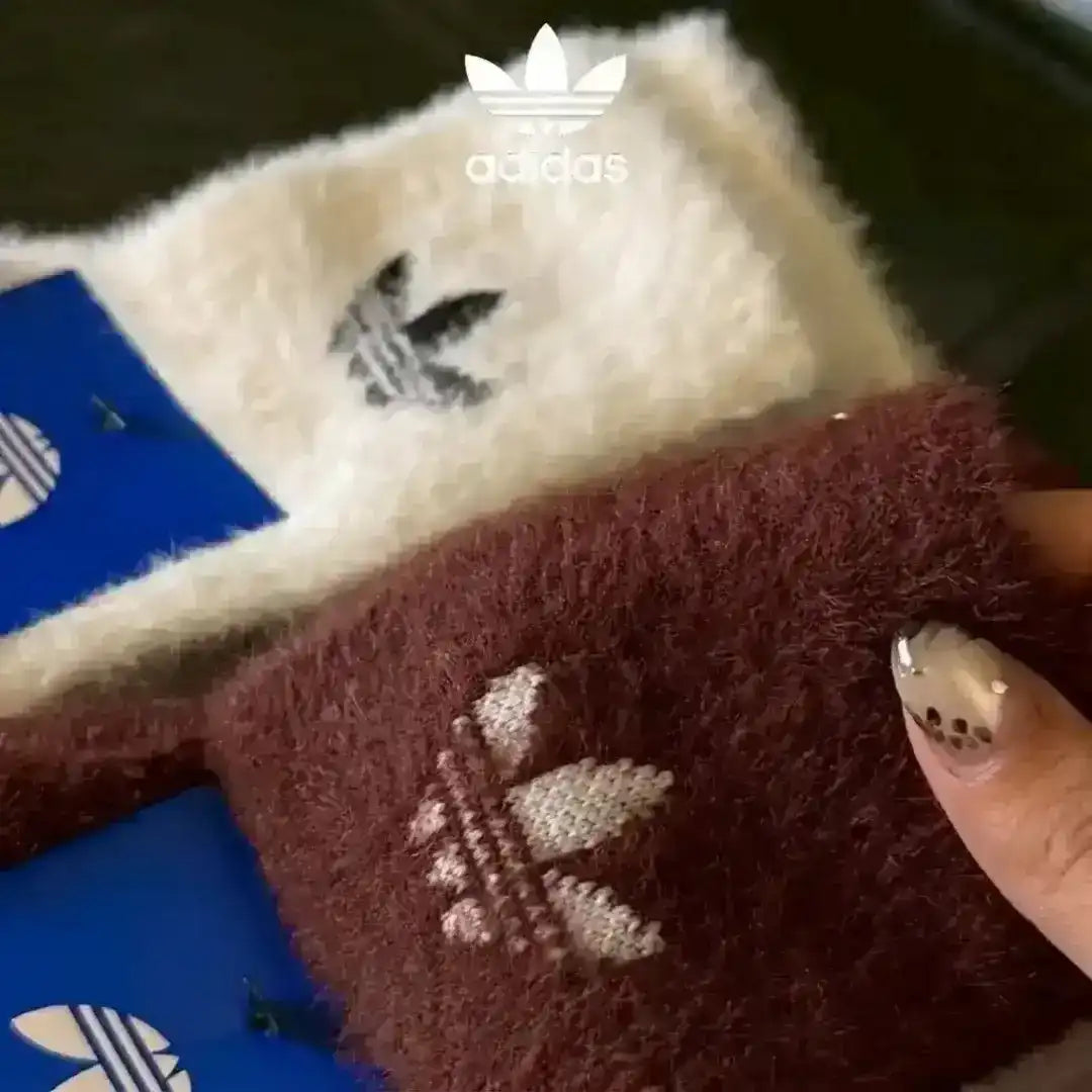 Adidas lounge socks made from thick, fluffy fabric for winter warmth, displaying the iconic Trefoil logo embroidered on black, cream, and reddish-brown options.