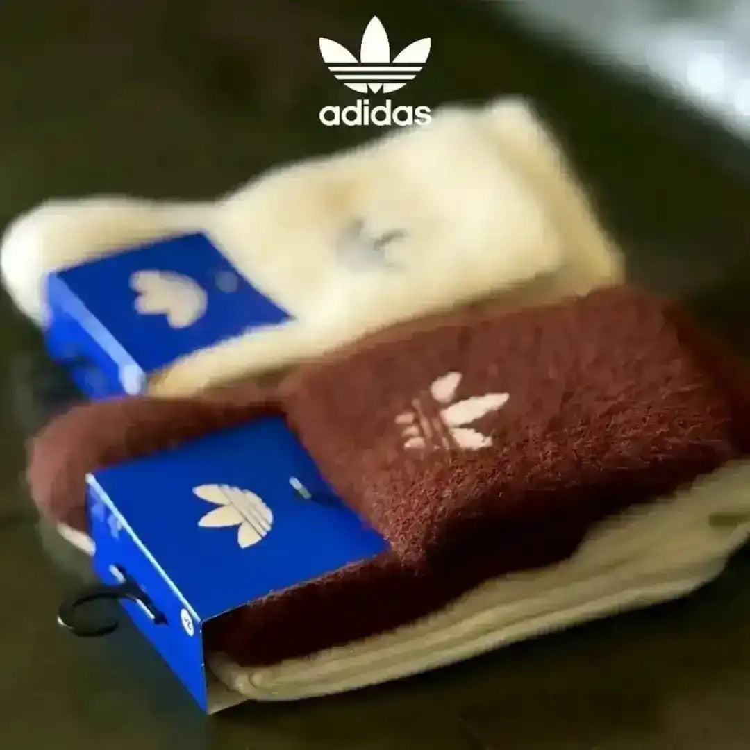 Textured Adidas fluffy knit socks resting on a green surface, designed for comfort and style with the signature Trefoil logo clearly visible on the ribbed cuffs.