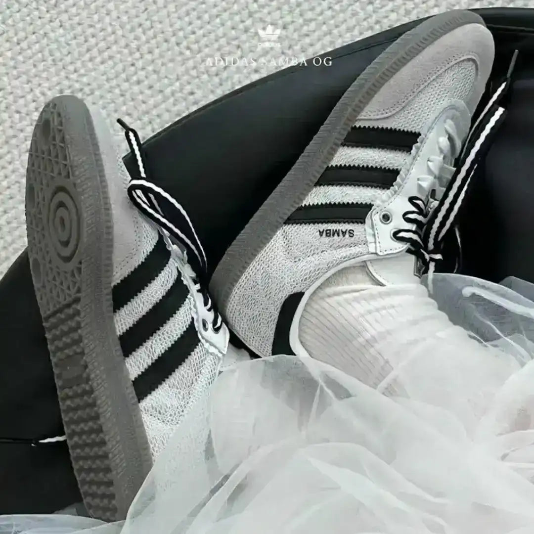 Top down view of custom white Adidas Samba OG sneakers featuring black and white striped ribbon laces and black flower patches with gold centers on the eyelets.
