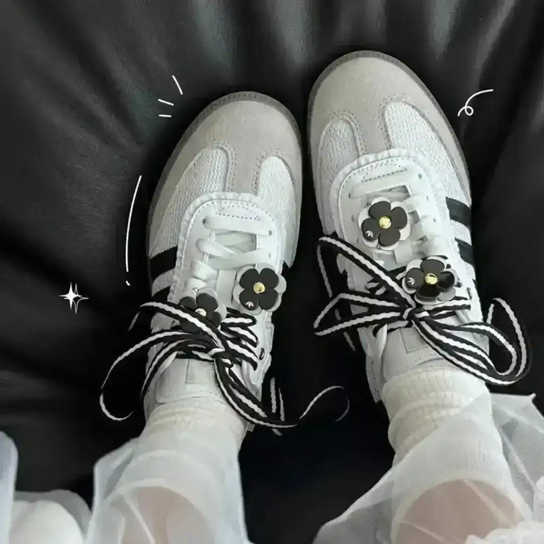White leather Adidas Samba OG trainers customized with black and white striped laces and black flower charms, offering a unique and stylish look.