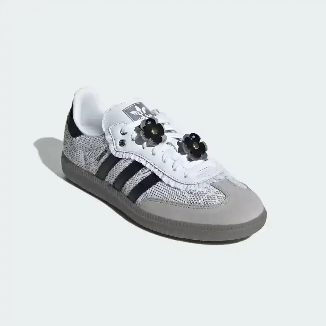 Top view of custom white Adidas Samba OG shoes featuring grey suede overlays, black stripes, and unique black and white striped laces adorned with flower patches.