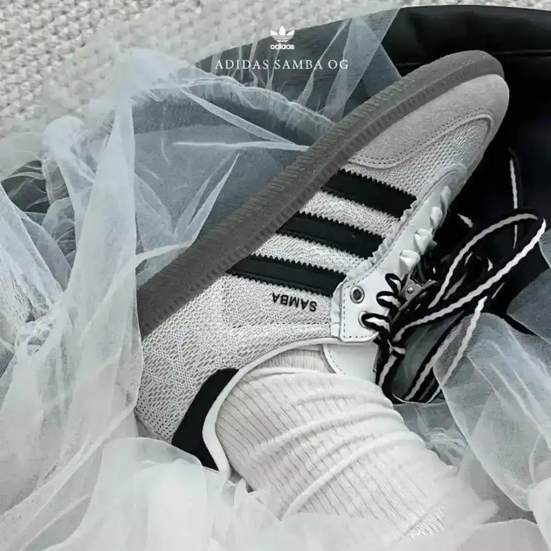 Fashion-forward custom Adidas Samba sneakers in white and grey, featuring unique black and white striped laces tied in bows and black flower details.