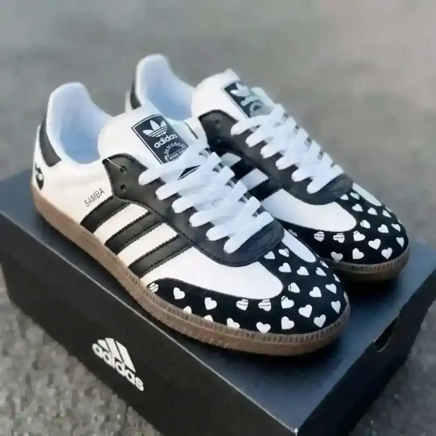Custom Adidas Samba sneakers in a classic white and black colorway, featuring a unique black suede toe cap with a white heart pattern and a heart logo on the heel.