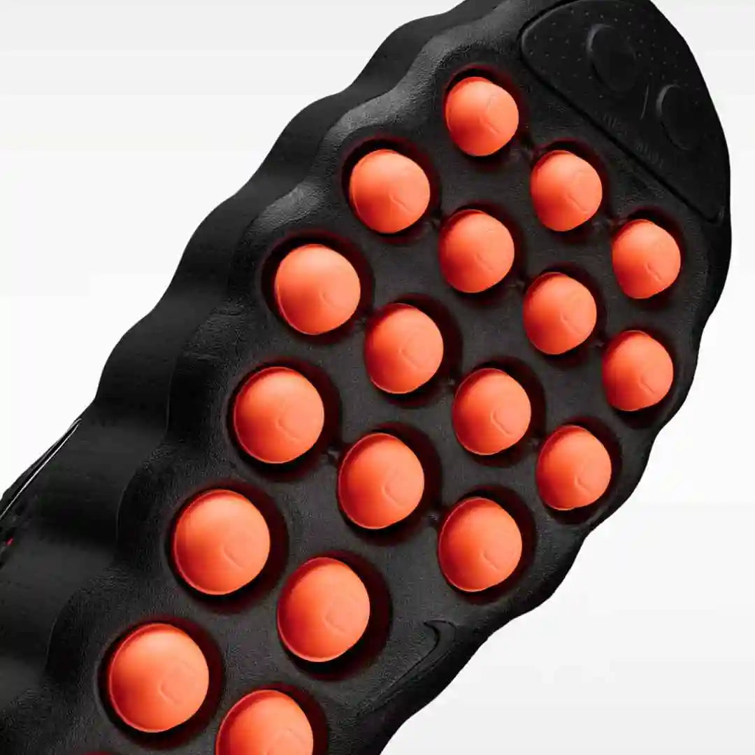 Black outsole with multiple round orange pods, bottom view.