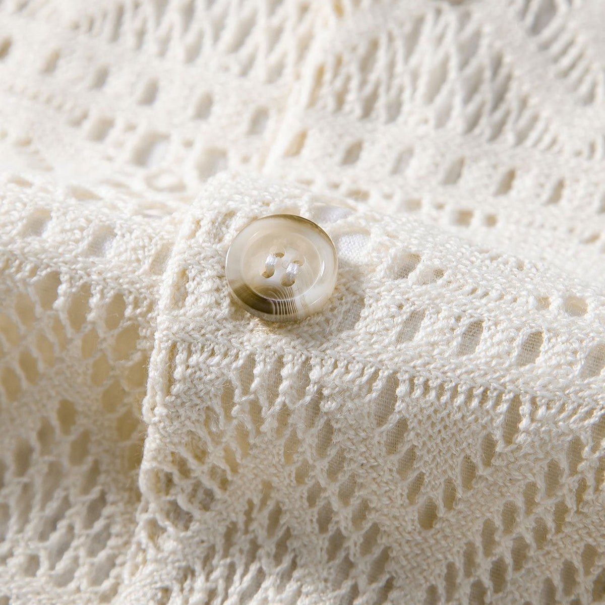 Close-up of a cream openwork shirt's collar, button and fabric.