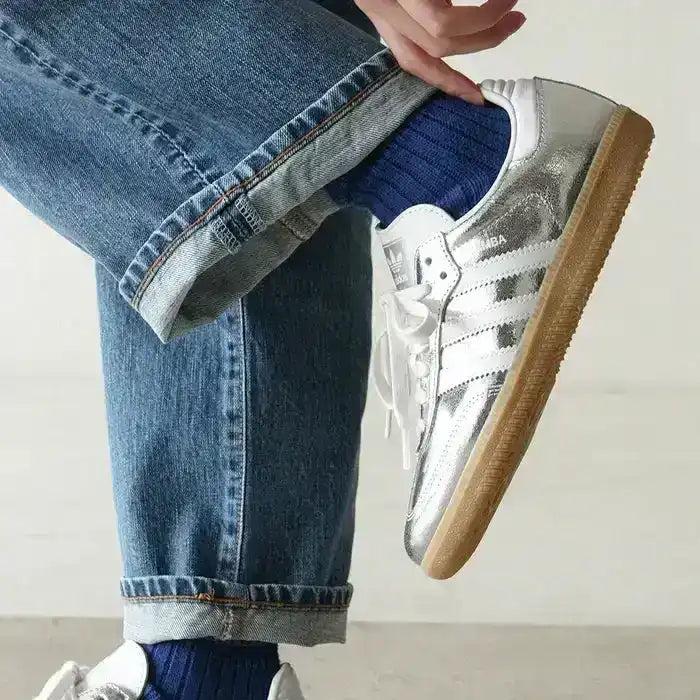 Silver-colored three-stripe low-top sneakers with gum soles.